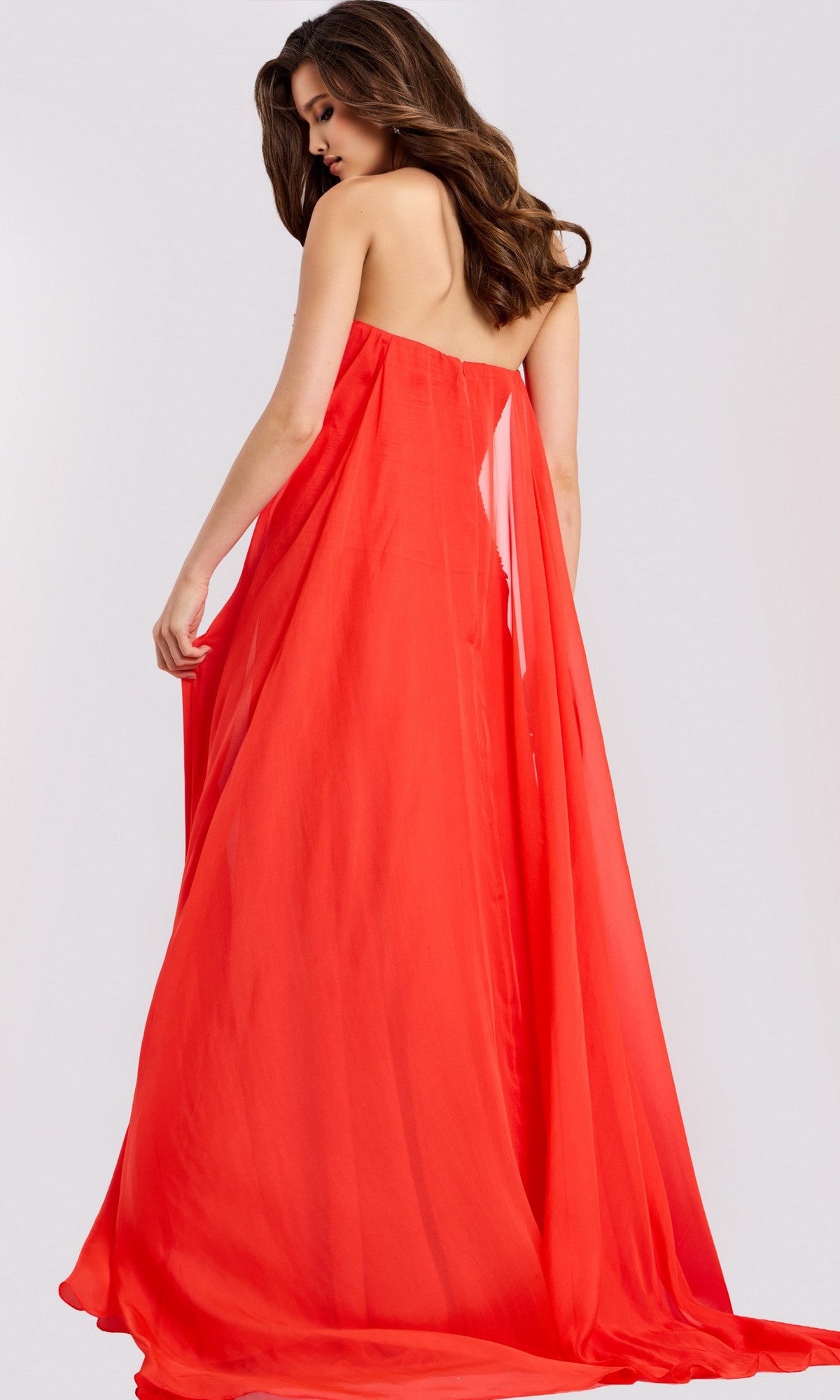A woman with long brown hair wears the Jovani 45269 long prom dress, featuring a strapless chiffon bodice and pleated A-line skirt, standing facing away and looking over her shoulder against a plain light background.